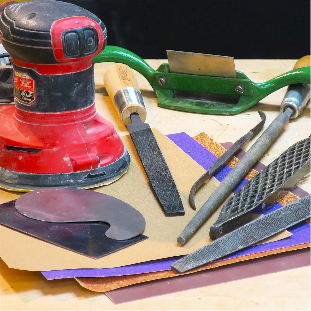 sandpaper, files, rasps, and card scrapers spread across a workbench